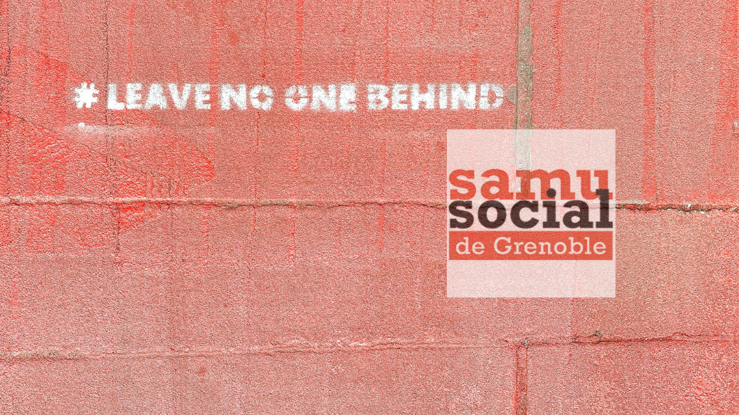 Mur en briques rouge avec une inscription blanche &quot;leave no one behind&quot; et le logo du samu social de Grenoble
